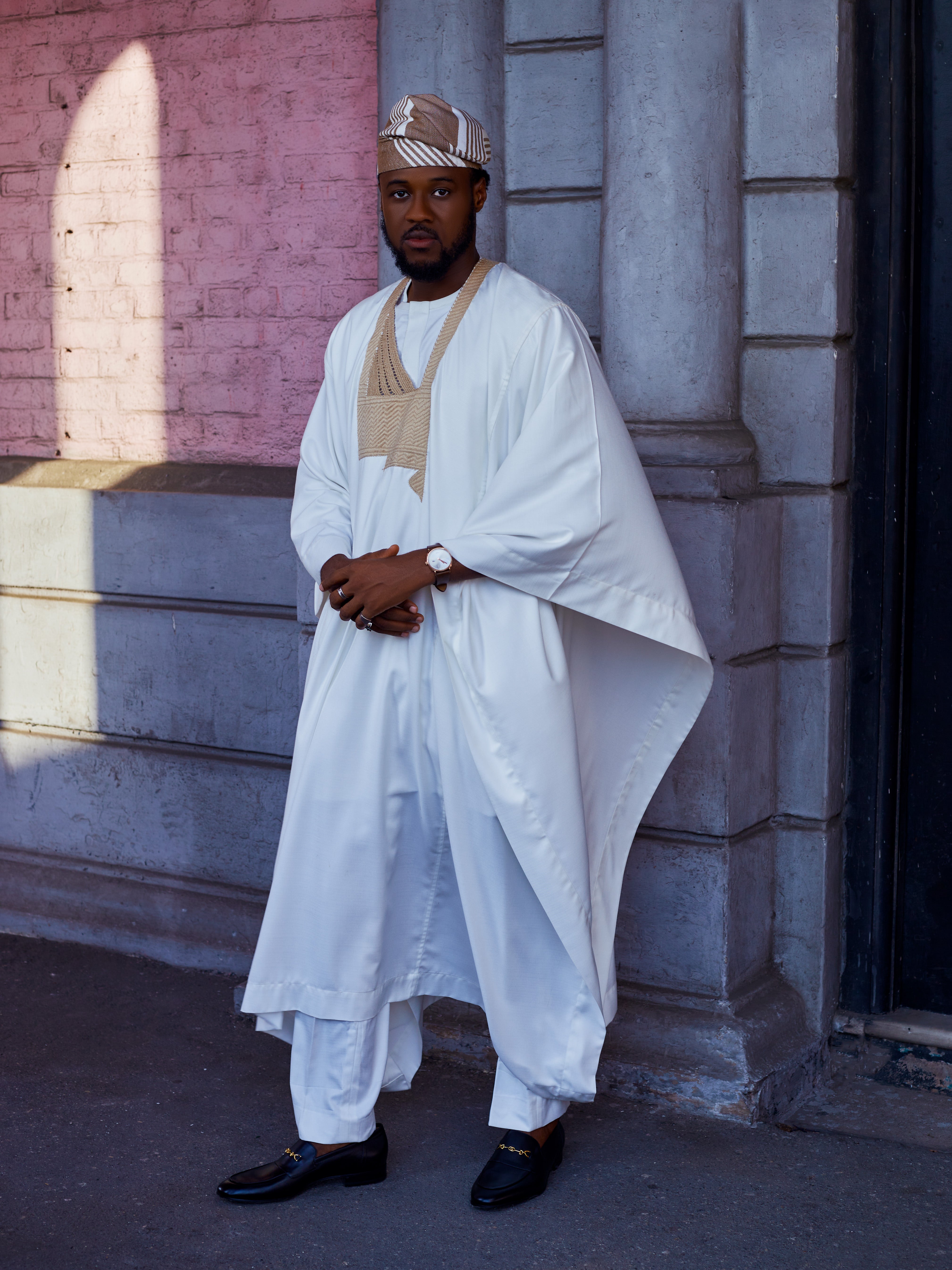 A man wearing an Agbada in off white colour and gold handknit embroidery with a matching Sanyan cap