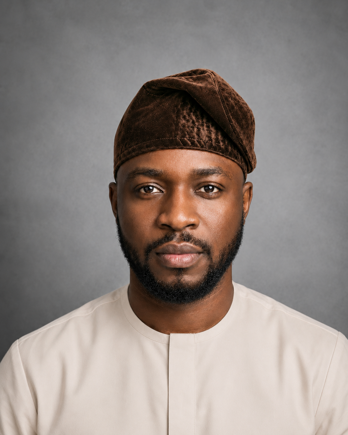 Male model wearing an Orí Adé coffee brown velvet Yoruba fila cap with a cream kaftan.