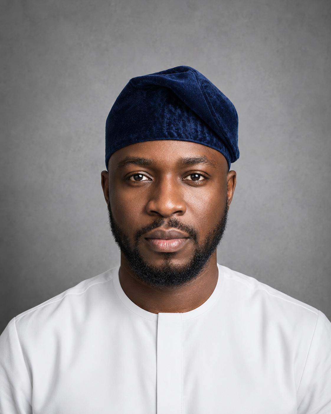 Male model wearing an Orí Adé navy blue velvet Yoruba fila cap with a white kaftan.